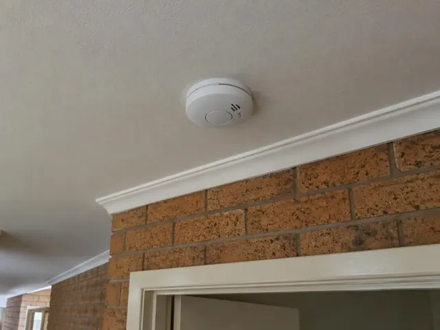 Ceiling-mounted smoke alarm above a brick interior wall and doorway in Labrador